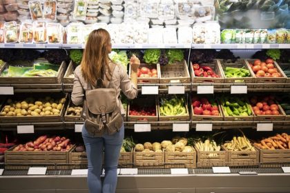 good looking woman standing front vegetable shelves choosing what buy